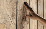 Primer plano de una mano tocando la superficie de un panel de madera de roble con vetas y nudos